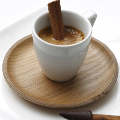 Chávena branca de café expresso com canela em pau num prato de madeira sobre superfície branca