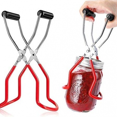 Abridor de frascos metálico com alças vermelhas e pretas a abrir um frasco de vidro com tampa prateada