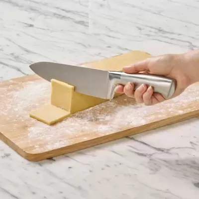 Faca metálica a cortar massa sobre tábua de madeira num balcão branco