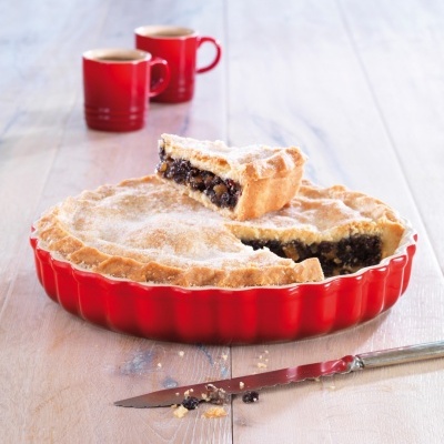 Tarte com recheio escuro numa forma vermelha com chávenas de café vermelhas ao fundo