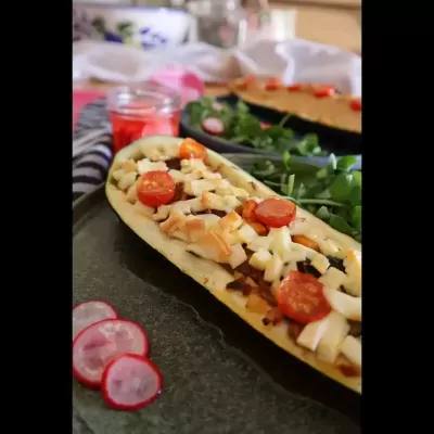 Metade de courgette recheada com tomate cherry e queijo ralado com rabanete e folhas verdes num prato preto