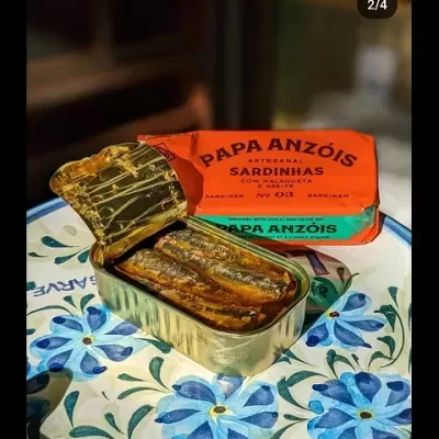 Lata de sardinhas PAPA ANZÓIS em lata dourada aberta e embalagem laranja num prato decorado.