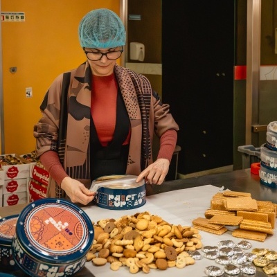 Mulher a abrir lata azul de bolachas numa mesa com bolachas e rebuçados