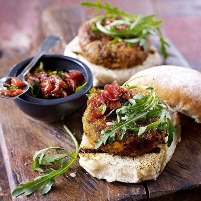 Dois hambúrgueres vegetarianos com rúcula e molho em pão ciabatta sobre tábua de madeira.