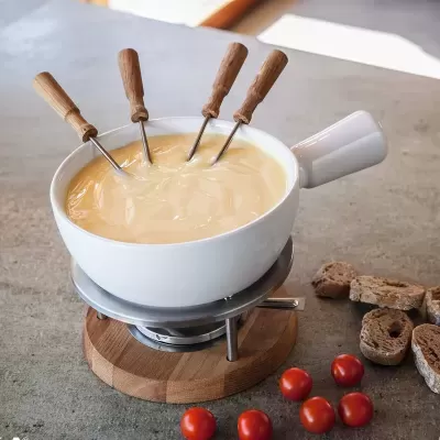 Panela branca de fondue com queijo, garfos de madeira, tomates cherry e pão integral numa superfície cinzenta.