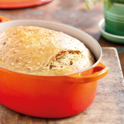 Pão caseiro num tacho laranja sobre tábua de madeira
