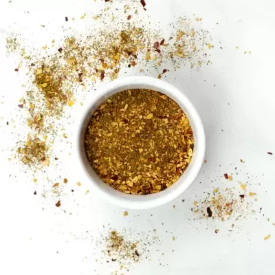 Recipiente branco com especiarias moídas amarelas e vermelhas, em superfície branca