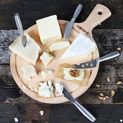 Tabuleiro de madeira com vários queijos, facas de queijo e fatia de pão com noz