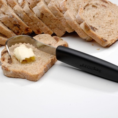 Fatia de pão integral com manteiga sendo espalhada com uma faca preta.
