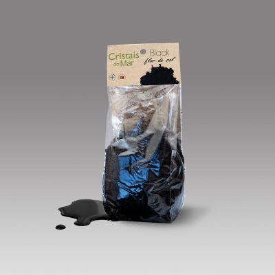 Pacote de flor de sal preta Cristais do Mar sobre fundo cinza com sal derramado.