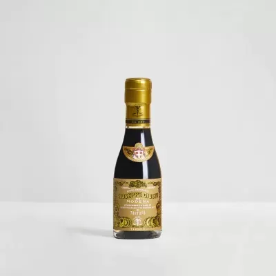 Garrafa pequena de vinagre balsâmico com rótulo dourado em fundo cinzento