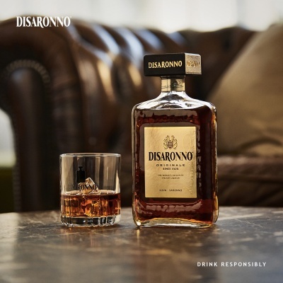 Garrafa de Disaronno e copo com bebida sobre mesa, sofá de couro ao fundo