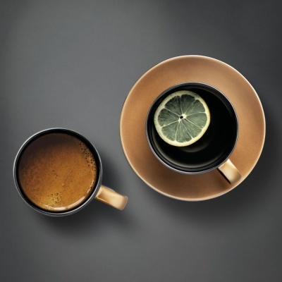 Duas chávenas castanhas com café e limão sobre fundo cinzento