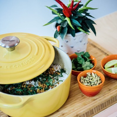 Caçarola amarela de ferro fundido com conteúdo e tigelas laranja com especiarias e ervas sobre bancada de madeira