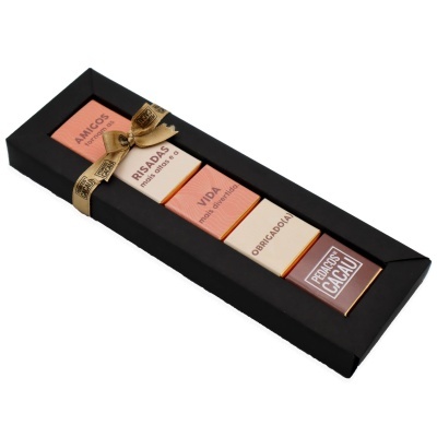 Conjunto de quatro barras de chocolate em embalagem rosa e creme dentro de caixa preta com fita dourada