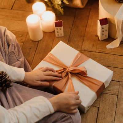 Presente embrulhado com fita cor de pêssego em chão de madeira com velas e miniaturas de casas