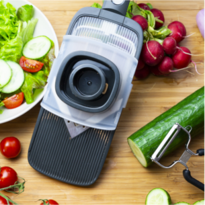 Mandolina de cozinha com legumes frescos sobre tábua de madeira