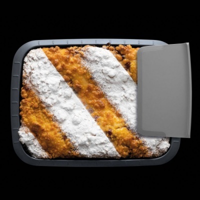 Tarte dourada com açúcar em pó em forma retangular numa forma cinzenta sobre fundo preto