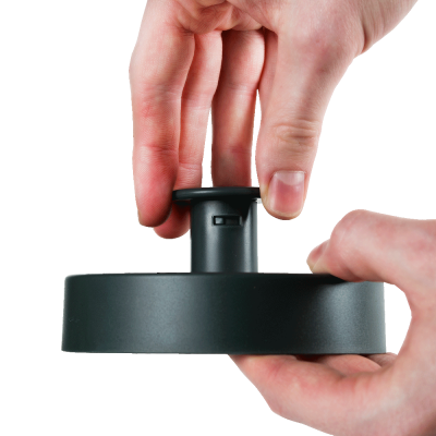 Objeto preto redondo com botão no centro segurado por duas mãos em fundo branco