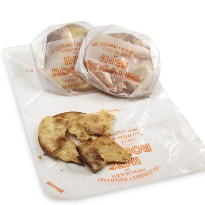 Tortas de aceite INÉS ROSALES em pacotes transparentes com uma torta aberta e quebrada sobre saco branco com texto laranja.