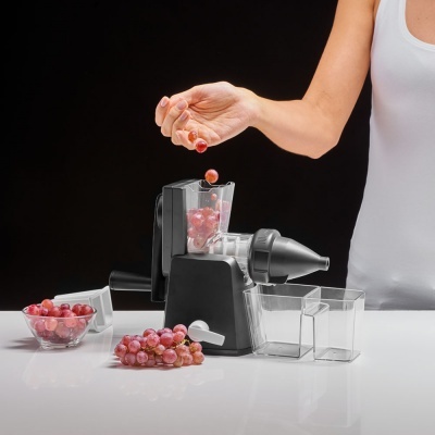 Máquina manual de fazer sumo com uvas vermelhas refletida numa mesa branca