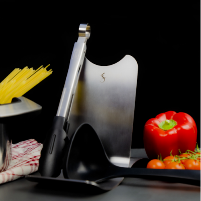 Utensílios de cozinha com pinça metálica e colher de pau com vegetais ao fundo