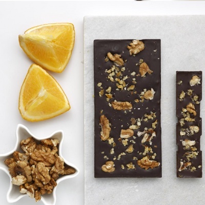 Barra de chocolate escuro com pedaços de nozes e gomos de laranja ao lado