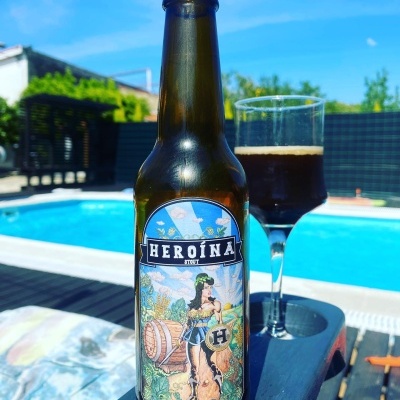 Garrafa de cerveja Heróina Beer com rótulo ilustrado e copo de cerveja escura junto a piscina