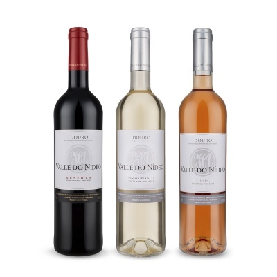 Três garrafas de vinho Valle Do Nideo com rótulos brancos, tinto com rolha vermelha, branco e rosé com tampas prateadas.
