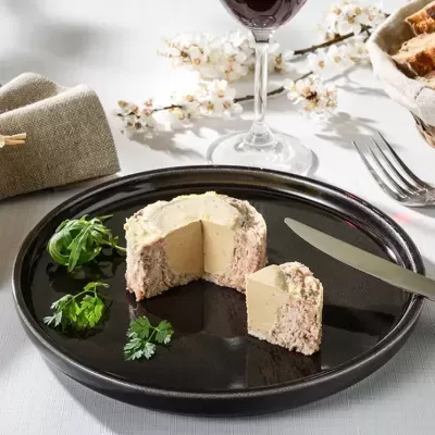 Queijo cremoso com crosta numa travessa preta, ervas, copo de vinho tinto e florezinhas ao fundo