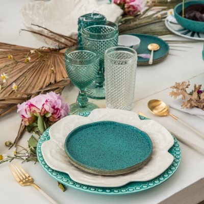 Conjunto de louça verde e creme com copos de vidro e talheres dourados numa mesa decorada com flores