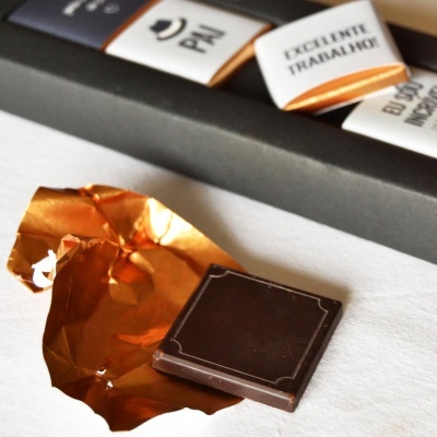 Quadrado de chocolate preto sobre papel dourado e fundo branco com embalagem preta