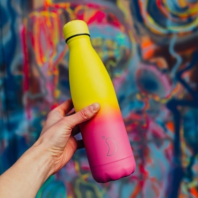 Garrafa térmica amarela e rosa com logo de pimento segurada em frente a grafite colorido