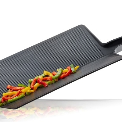 Tabuleiro de cozinha preto com textura riscada e pimentos coloridos cortados.