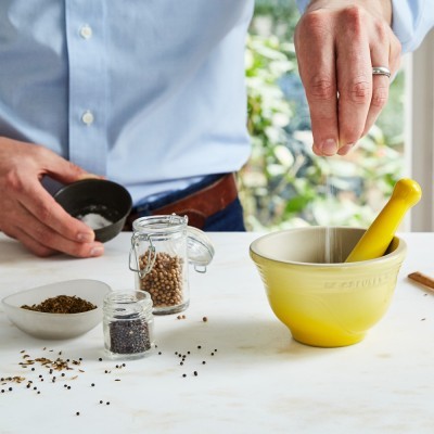 Pessoa a temperar especiarias perto de almofariz amarelo LE CREUSET numa mesa branca