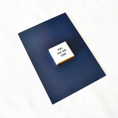 Caixa pequena branca com texto em cima de papel azul escuro sobre superfície branca