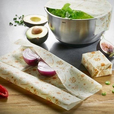 Folhas de cera de abelha com padrão floral a envolver alimentos e taça metálica em bancada de madeira