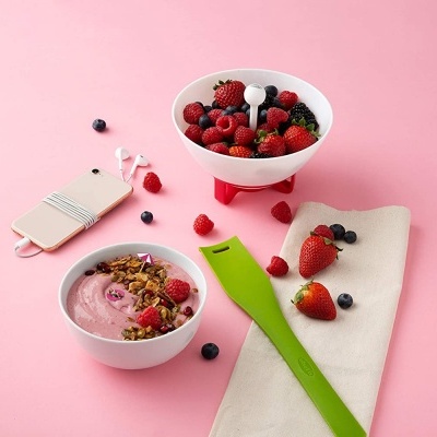 Taças brancas com iogurte rosa, granola e frutos vermelhos em superfície rosa