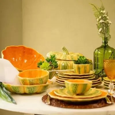 Conjunto de loiça verde e laranja com plantas e garrafa verde numa mesa redonda branca