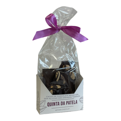 Pacote de chocolate negro com amêndoa torrada, embalado em bolsa transparente com fita roxa, numa caixa branca da Quinta da Patela