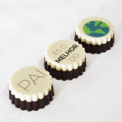Três bombons com chocolate branco e escuro, um com desenho do planeta Terra e dois com texto em português.