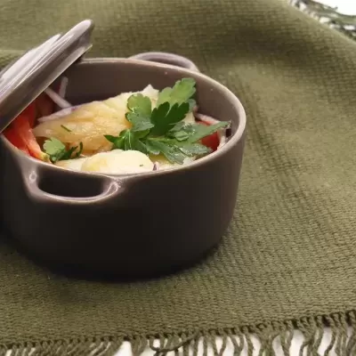 Caçarola de cerâmica castanha com comida e salsa em pano verde