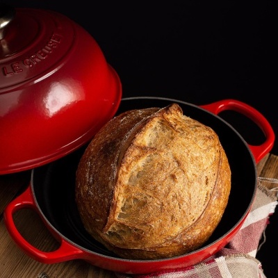 Pão dentro de caçarola vermelha de ferro fundido LE CREUSET sobre madeira e pano xadrez.
