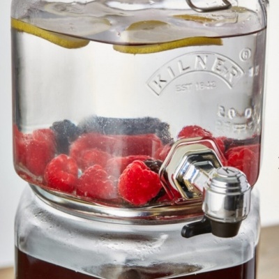 Recipiente de vidro com torneira contendo água, limão e framboesas