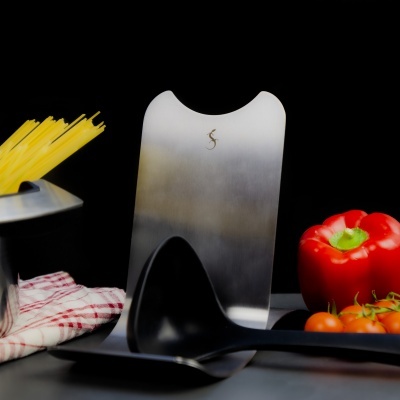 Utensílios de cozinha com espátula metálica, pegador preto, esparguete, pano vermelho e branco, pimento e tomates.