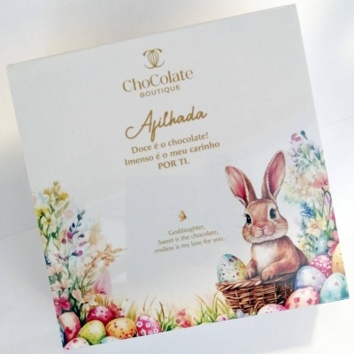 Caixa branca de chocolate com coelho, ovos coloridos e texto em dourado e castanho