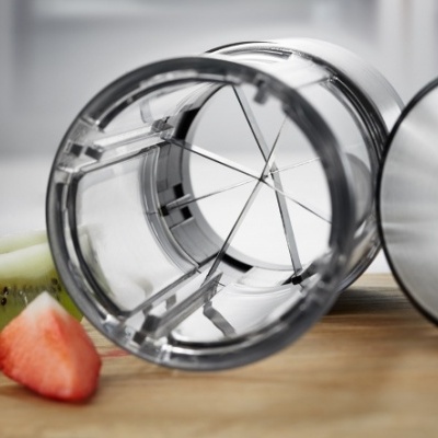 Cortador fatiador com lâminas em metal e corpo plástico transparente junto a frutas