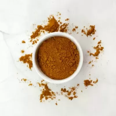 Recipiente branco com pó castanho e pó espalhado à volta em superfície clara