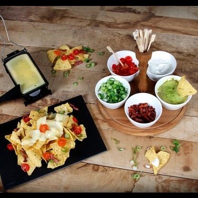 Mesa com nachos, queijo fundido e molhos variados.