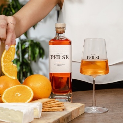 Garrafa e taça de licor PER SE com laranjas, queijo e bolachas numa tábua de madeira